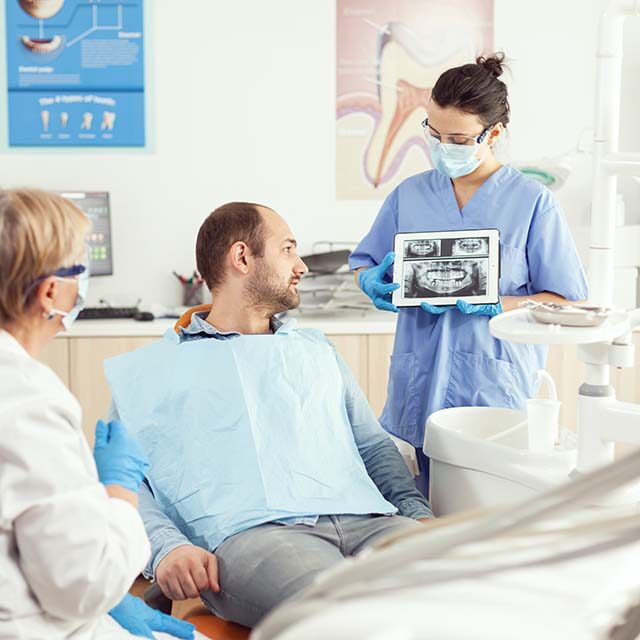 sick-man-sitting-stomatological-chair-listening-doctor-while-looking-tablet-dental-clinic